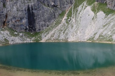 Trentino, İtalya - 29 Temmuz 2025: Piz Boe 'nun görkemli panoramik manzarası ve çevreleyen Dolomite tepeleri, yemyeşil vadiler ve açık mavi bir gökyüzü altında dağınık kar. Boe Gölü 'ne güzel bir manzara, ve su üzerinde gökyüzü yansıması..
