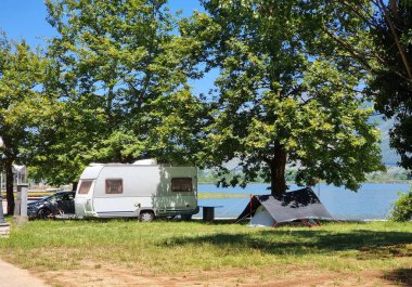 caravan car  and trailer  tent by the lake and green platanus trees in summer holidays adventure clipart