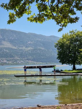 Kürek çeken kürekçiler yaz mevsiminde ioannina ağaçlarının altında Pamvotis Gölü 'nde antrenman yapıyorlar.