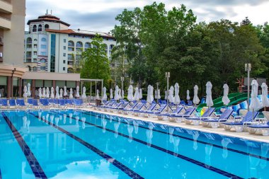 Swimming pool with empty loungers and closed umbrellas at luxury hotel . High quality photo