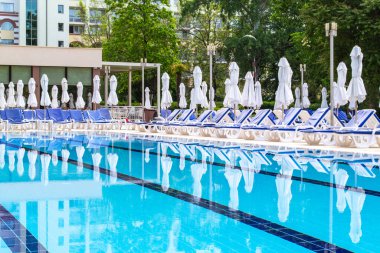 Swimming pool with empty loungers and closed umbrellas at luxury hotel . High quality photo