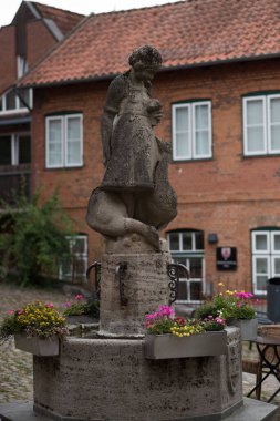 Yıpranmış taş bir heykel yıpranmış beton bir kaide üzerinde durur, bir kuşu ya da küçük bir hayvanı nazikçe tutan çocuk benzeri bir figürü tasvir eder. Heykelin, eski yüzeyi ve zamanla yumuşayan karmaşık ayrıntılarıyla klasik bir kırsal cazibesi var.. 