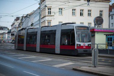  Modern, eklemli tramvay Viyana 'da sokak boyunca seyahat ediyor. Tramvay pürüzsüz, alçak tabanlı, özellikle koyu gri renkli, yanında belirgin kırmızı şeritli, Viyana 'nın toplu taşıma sisteminin bir özelliği.