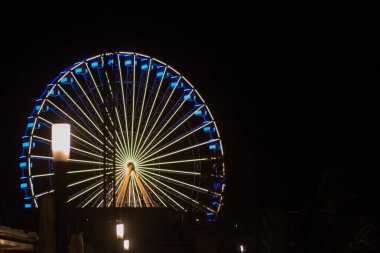 Bir dönme dolap, Almanya 'nın Grmitz kentindeki renkli ışıklarla aydınlatılmış gece gökyüzü ve denizin arka planında bir eğlence gezisi.