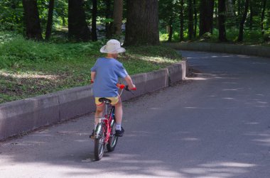 Yağmurlu bir günde, taze yeşil ağaçlar ve ıslak kaldırımlarla çevrili küçük bir bisiklete biniyor. Ukrayna, Kyiv 01.05.2014
