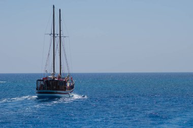 Kıbrıs Rum Kesimi ve turistler yaz gezisi sırasında bir zevk gemisinde kameraya el sallıyor, parlak güneşli gökyüzü ve turkuaz okyanus dalgaları.