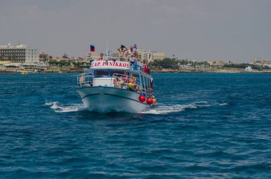 Kıbrıs Rum Kesimi, bir turist teknesinin üst güvertesinde dinlenen bir grup tatilci, neşeli atmosfer ve manzaralı kıyı manzarası