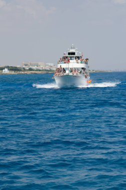 Bir grup tatilci bir turist teknesinin üst güvertesinde dinleniyor, neşeli bir atmosfer ve manzaralı sahil manzarası.