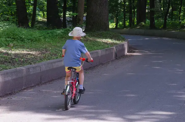 Yağmurlu bir günde, taze yeşil ağaçlar ve ıslak kaldırımlarla çevrili küçük bir bisiklete biniyor. Ukrayna, Kyiv 01.05.2014