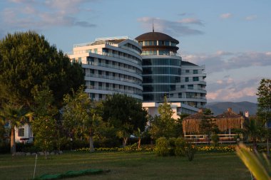 Çarpıcı derecede modern bir otel, Türk kıyılarında yemyeşil bir otelle çevrilidir. Kıvrımlı yapısı, hafif tonlu cephesi ve yuvarlak çatısı ona farklı bir görünüm kazandırıyor..