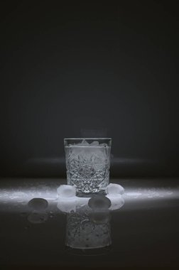 Etrafında kristal su bardağı, buz küpleri ve su damlalarının dikey görüntüsü, koyu bir arkaplan üzerine..