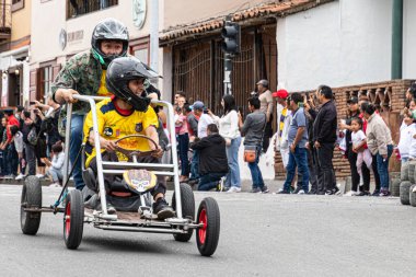 Cuenca, Ekvador - 3 Kasım 2022: Bir adam Cuenca Bağımsızlık Günü kutlamalarında kalabalığın kendisine tezahürat etmesi üzerine ev yapımı sabun kutusu arabasıyla (coche de madera) yarışıyor.