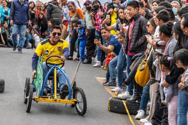 Cuenca, Ekvador - 3 Kasım 2022: Bir adam Cuenca Bağımsızlık Günü kutlamalarında kalabalığın kendisine tezahürat etmesi üzerine ev yapımı sabun kutusu arabasıyla (coche de madera) yarışıyor.