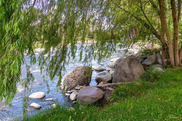 Big stones on the river bank in the shade of willow tree. Mountain river Yanuncay in the valley of city Cuenca, El Paraiso Park, Ecuador