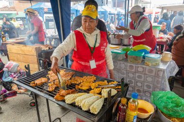 Cuenca, Ekvador - 7 Temmuz 2024 Cuenca kentinde et festivali. Bir kadın ızgarada tavuk bifteği ve mısır koçanı pişiriyor. Sokak yemeği.
