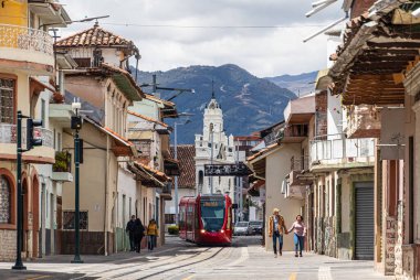 Cuenca, Ekvador - 12 Aralık 2022 Gran Kolombiya caddesi ve Corazn De Jess kilisesi. Modern kırmızı tramvay, UNESCO 'nun Dünya Mirası sahası Cuenca kentinin tarihi merkezinden geçiyor.