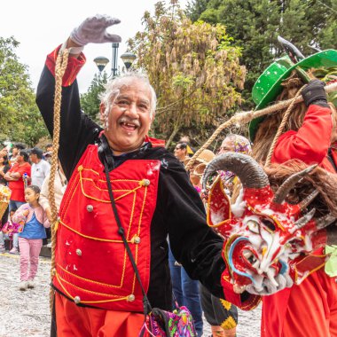 Cuenca, Ekvador - 10 Şubat 2024 Cuenca 'nın tarihi merkezinde karnaval geçidi. Kırmızı şeytan maskeli yaşlı bir adam. Geleneksel olarak, geçit töreni katılımcıları ve seyirciler köpük püskürtür.