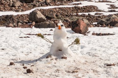 Chimborazo yanardağının karlı yamacında duran, havuç burunlu, taş gözlü, güneş gözlüklü ve dağ çalılığından (And 'ların çiçeği) yapılmış sopa kollu bir kardan adam. And Dağları, Ekvador