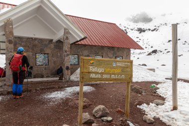 Chimborazo, Ekvador - 20 Nisan 2025: Karlı güneşli Chimborazo yanardağı. Binanın yakınındaki turistler 'Whymper Barınağı' nı imzaladı. Yükseklik: 5000 metre.