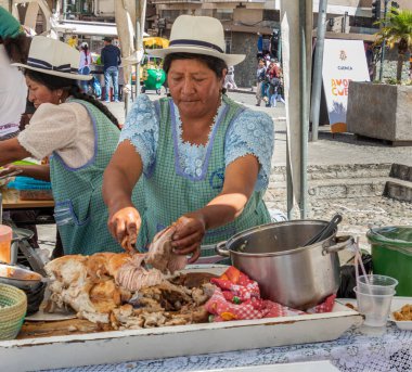 Cuenca, Ekvador - 26 Ekim 2024: Cuenca 'nın tarihi merkezinde zanaat fuarı. Keçuva kadınları ziyaretçilere tipik sokak yemekleri satarlar Hornado (veya Chancho), ki bu da tamamen kızarmış bir domuz..