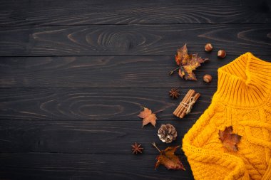 Sonbahar arkaplanı düzleşmişti. Örgü süveter, dökülen yapraklar ve ahşap arka plandaki baharatlar..