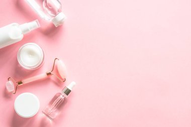 Natural cosmetics on pink. Skin care product, cream, soap serum, jade roller. Flat lay image with copy space.
