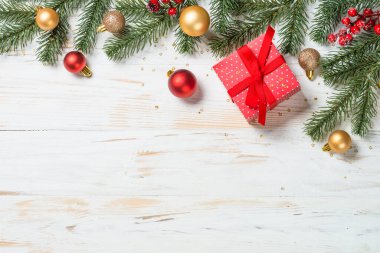Kırmızı kurdeleli ve Noel süslemeli Noel hediyesi kutusu. Beyaz ahşap masadaki en üst manzara.