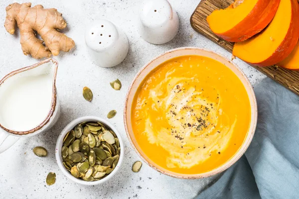stock image Pumpkin soup puree with cream and seeds in the bowl. Top view image at white table.