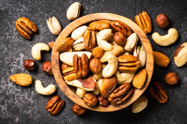 Koyu taş masadaki ahşap kasede fındık çeşitleri. Kaju, fındık, badem, Brezilya fındığı ve ceviz. Üst görünüm.