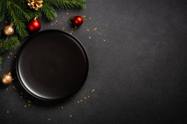 Siyah tabaklı Noel masası, altın çatal bıçak takımı ve tatil süslemeleri. Siyah üzerine üst görünüm.