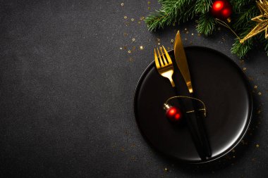 Siyah tabaklı Noel masası, altın çatal bıçak takımı ve tatil süslemeleri. Siyah üzerine üst görünüm.