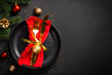 Siyah tabaklı Noel masası, altın çatal bıçak takımı ve tatil süslemeleri. Kopyalama alanı olan siyah üzerine üst görünüm.