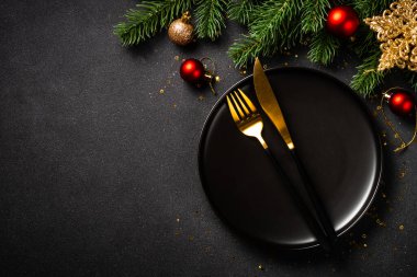 Siyah tabaklı Noel masası, altın çatal bıçak takımı ve tatil süslemeleri. Siyah üzerine üst görünüm.