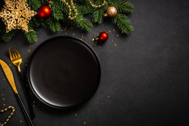 Siyah tabaklı Noel masası, altın çatal bıçak takımı ve tatil süslemeleri. Siyah üzerine üst görünüm.