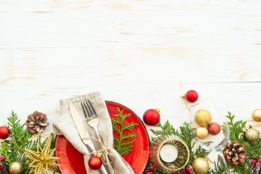 Noel sofrasında el işi tabağı, çatal bıçak takımı, mum ve Noel süslemeleri beyaz ahşap arka planda. Metin için boşluk olan üst görünüm.