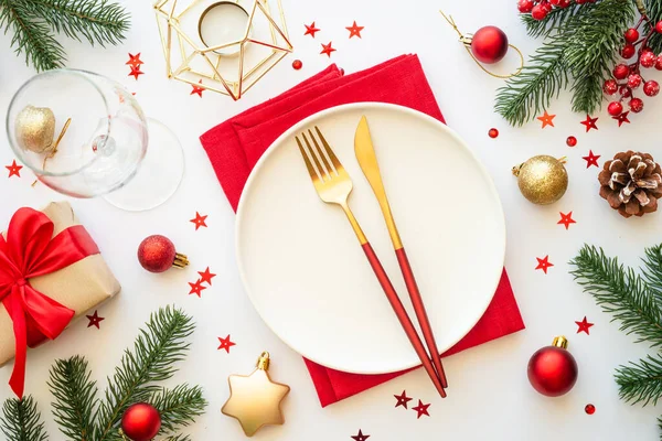 Christmas food, christmas table setting with white plate, golden cutlery and christmas decorations on white background. Top view.