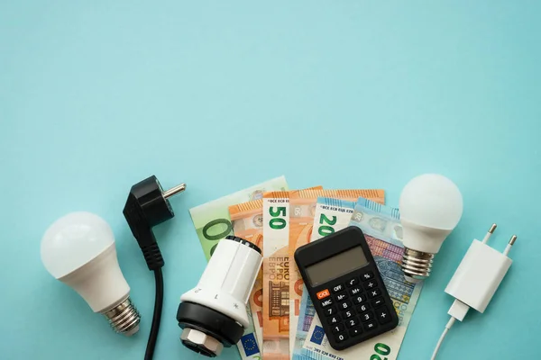 stock image Utility payments. Electricity and heating savings concept. Led lamp, thermostat, calculator and electric cable at blue. Top view with copy space.