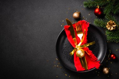 Siyah tabaklı Noel masası, altın çatal bıçak takımı ve tatil süslemeleri. Siyah üzerine üst görünüm.