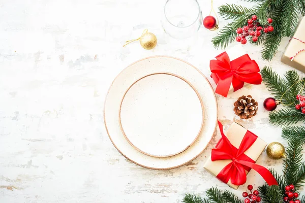 Christmas food, christmas table setting with white plate, golden cutlery and christmas decorations on white wooden background. Top view with copy space.