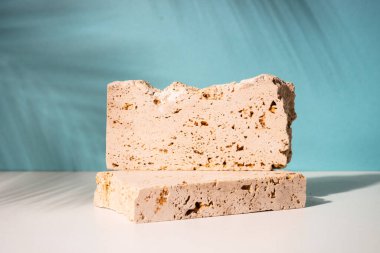 Travertine podyumu mavi arka planda kozmetik ürünler sunumu için. Palmiye yaprakları gölge.