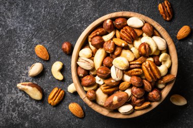 Koyu taş masadaki ahşap kasede fındık çeşitleri. Kaju, fındık, badem, Brezilya fındığı ve ceviz. Kopyalama alanı olan üst görünüm.