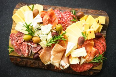 Antipasto. Peynir ve et - jamon, zeytinli salam ahşap servis panosunda, siyah arka planda. Üst görünüm.