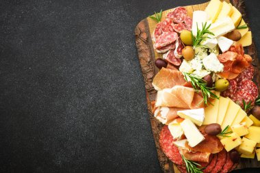 Antipasto. Peynir ve et - jamon, zeytinli salam ahşap servis panosunda, siyah arka planda. Kopyalama alanı olan üst görünüm.