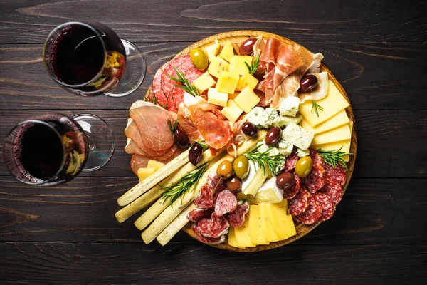 Antipasto at wooden serving board. Cheese and meat - jamon, salami with olives at wooden table. Top view with copy space.