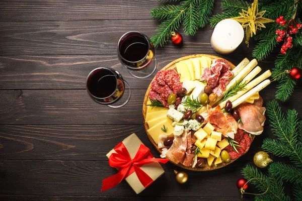 Christmas food Antipasto with red wine and presents. Cheese and meat with olives at serving board. Romantic christmas or New Year dinner for couple.