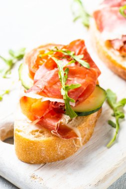 Beyaz arka planda kesme tahtasının üzerinde prosciutto ve roka ile sandviç açın. Resmi kapat.