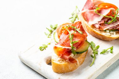 Beyaz arka planda kesme tahtasının üzerinde prosciutto ve roka ile sandviç açın. Kapat..