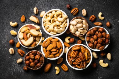 Fındık çeşitleri kaselerde. Kaju, fındık, ceviz, badem, Brezilya fındığı ve fıstık. Siyah taş masadaki en üst görünüm.