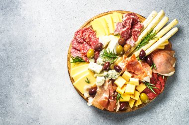Antipasto tabağı. Peynir ve et - jamon, salam, ahşap tahtada taş zeminde zeytin. Üst görünüm.