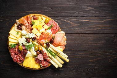 Tahta servis tahtasındaki Antipasto. Peynir ve et - jamon, ahşap masada zeytinli salam. Kopyalama alanı olan üst görünüm.